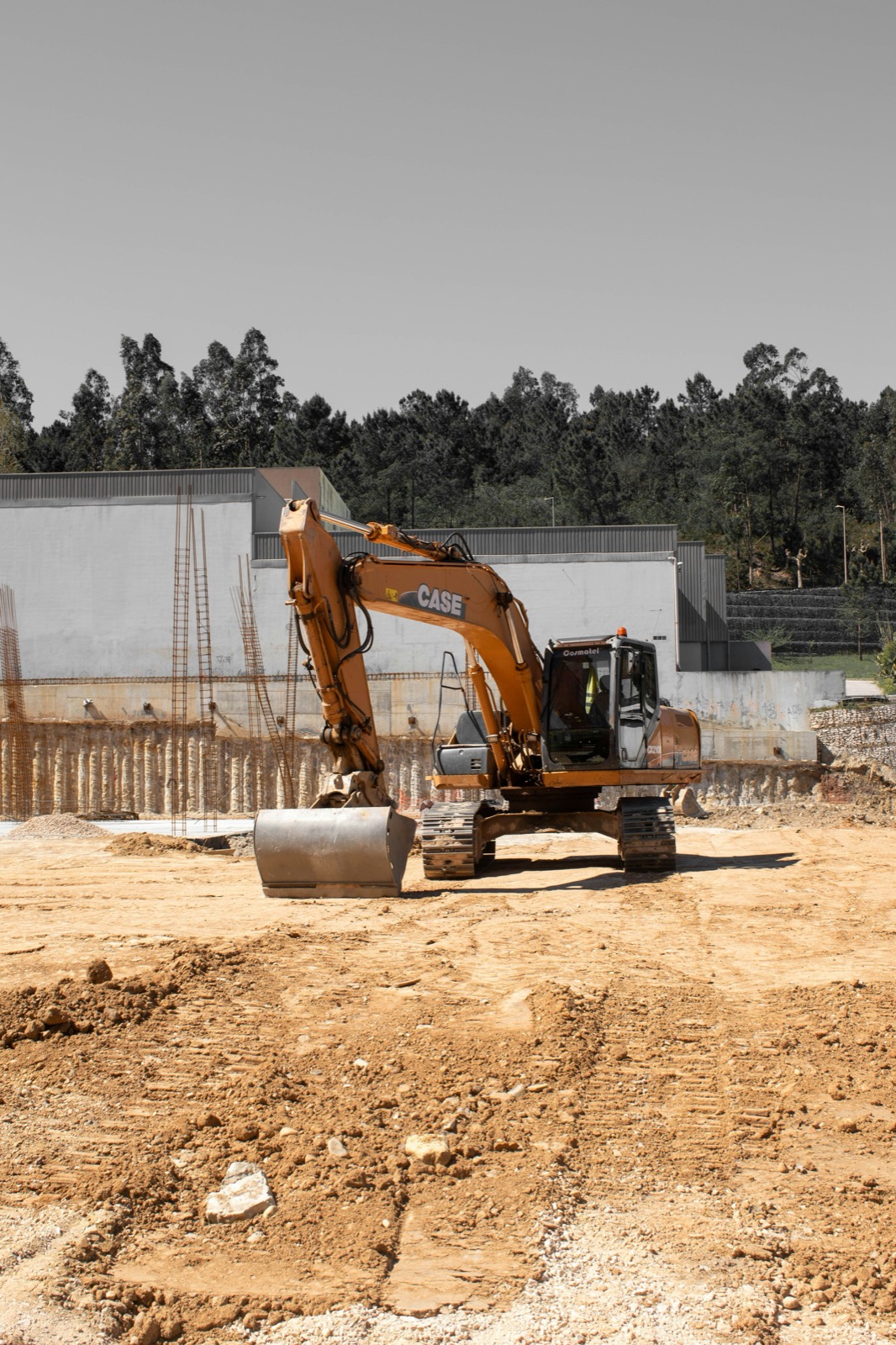 Excavator on a graded pad beside a retaining wall and rebar