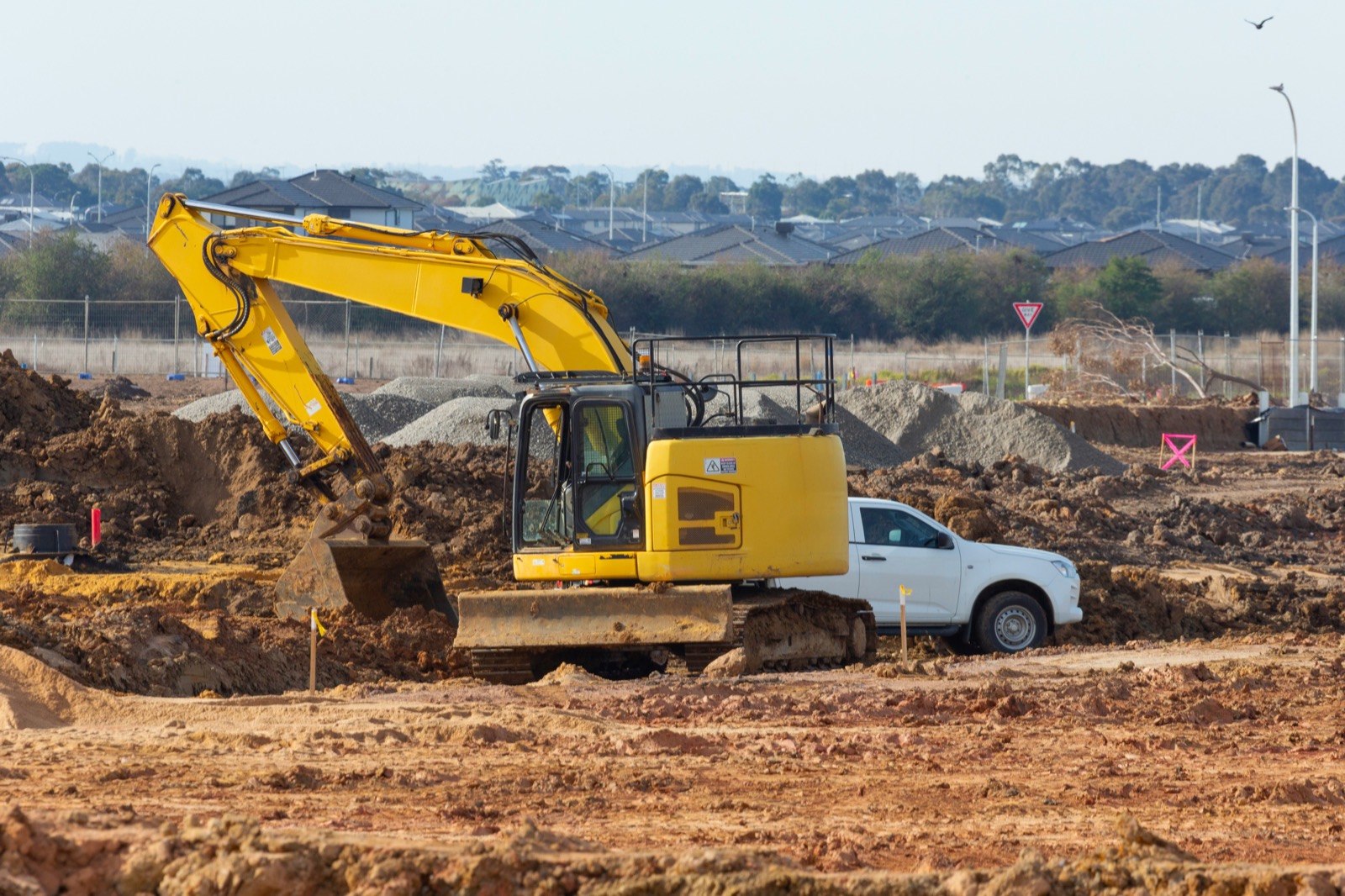 Yellow excavator preparing a residential lot with homes in the background