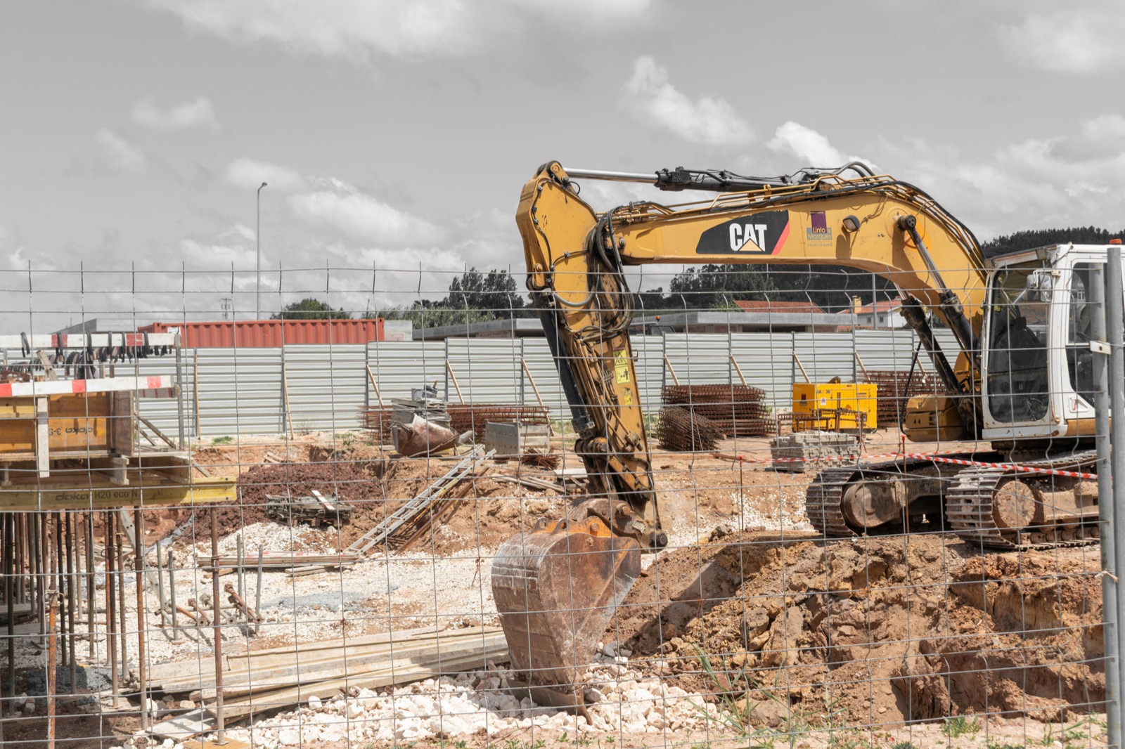 Yellow excavator working inside a fenced construction site with formwork and rebar
